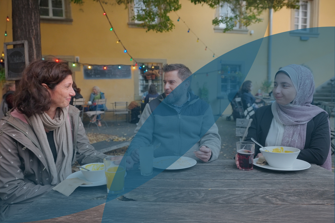 One man and two women having a conversation while they sit outside on a table at a cafe for lunch.