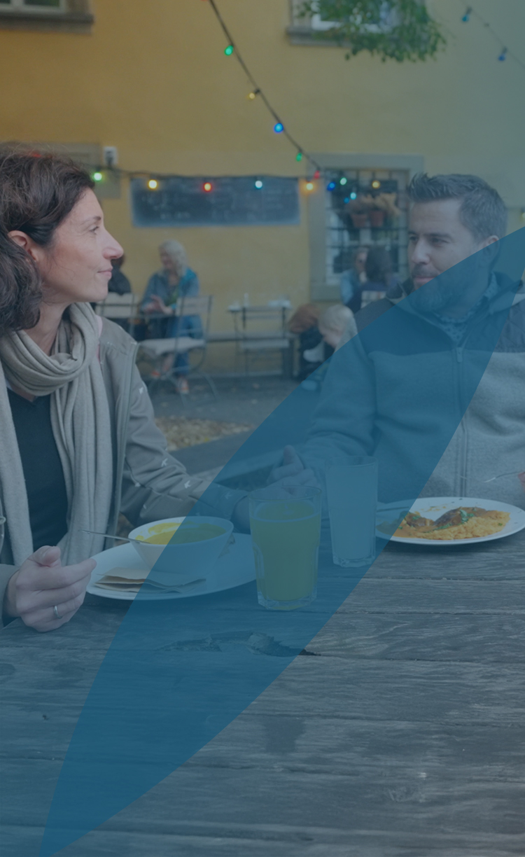 One man and two women having a conversation while they sit outside on a table at a cafe for lunch.