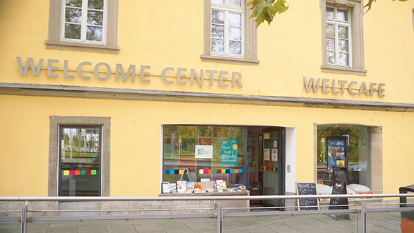 Yellow building with two entrances and with the Welcome Center and Welt Cafe Logo attached on the walls