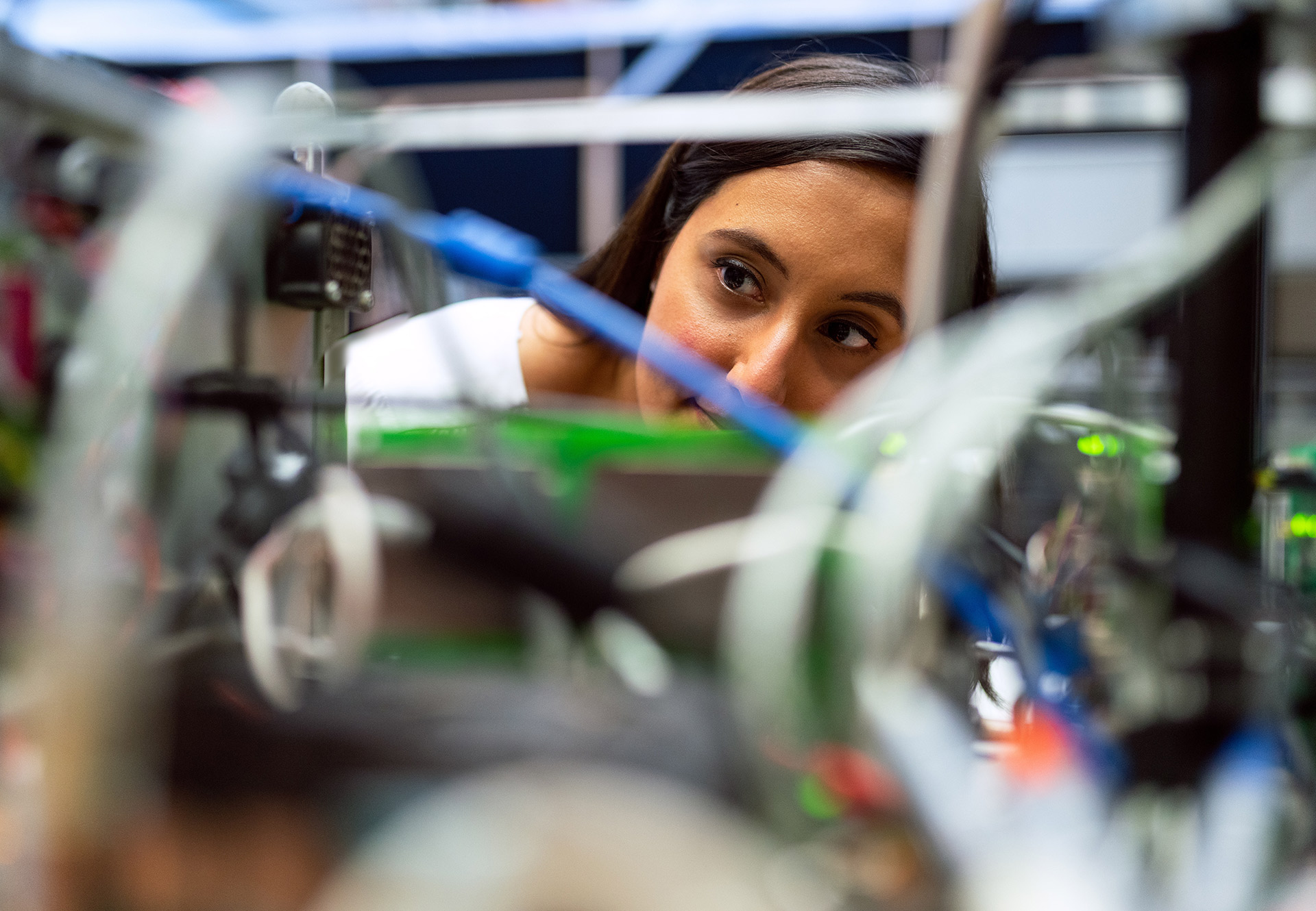 A female engineer looks at her work, which is blurred in the foreground and consists of many cables plugged into various connectors.