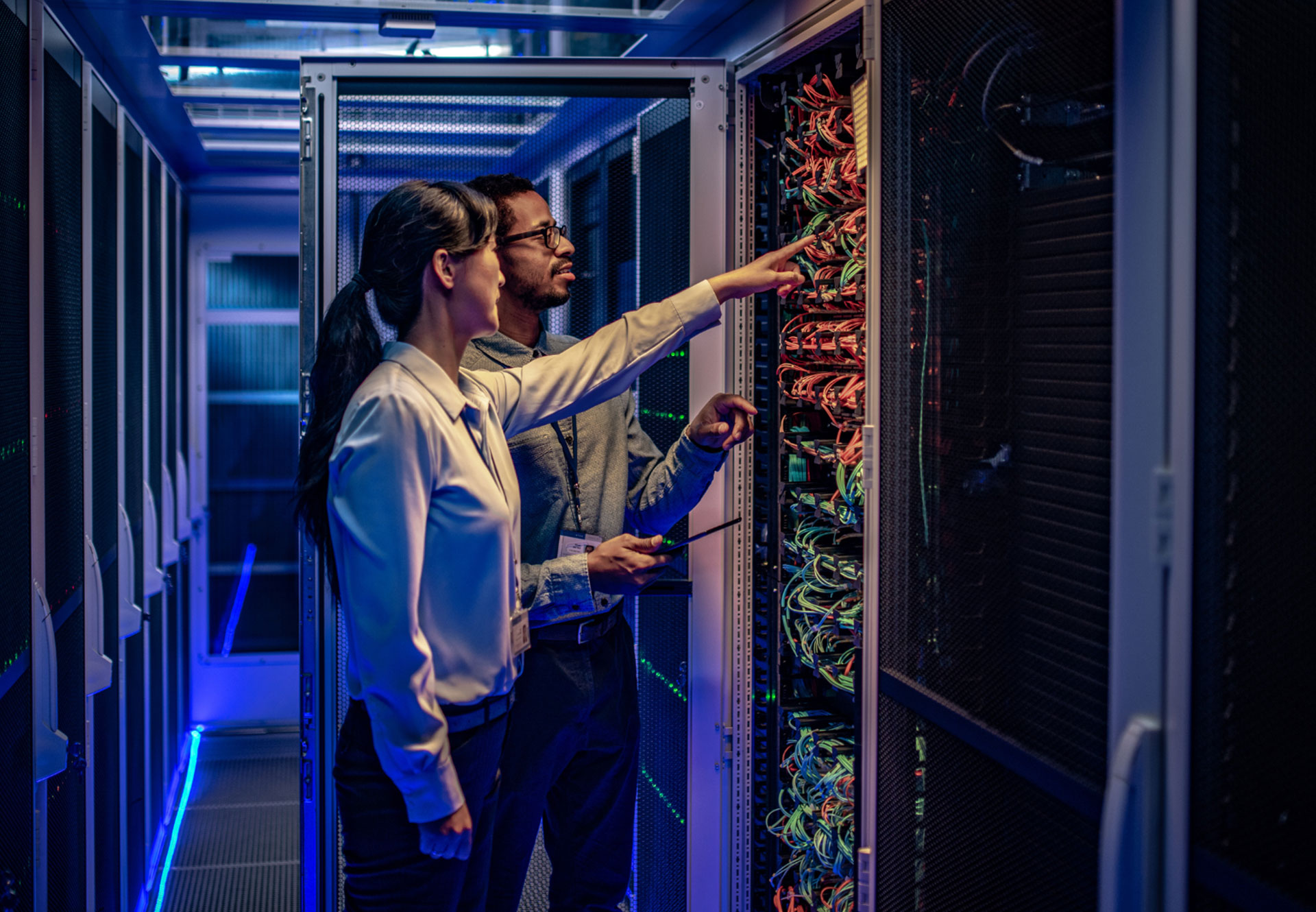 A man and a woman stand in front of an IT server and check the circuits