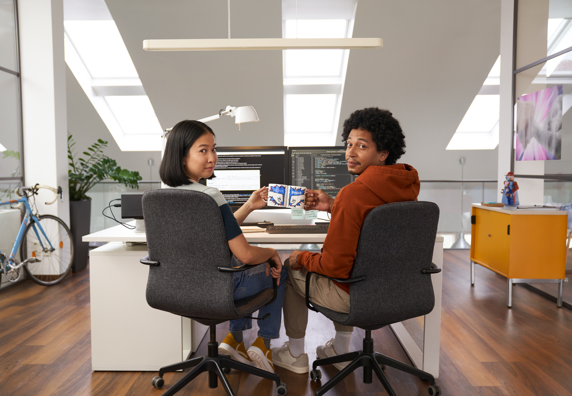 two co-workers sitting in front of a computer with their heads turned towards the camera