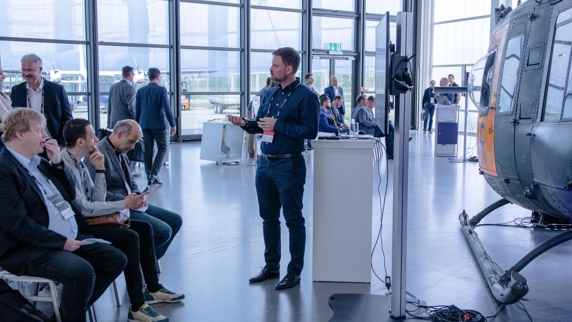 A member of STARTUP AUTOBAHN talking in front of a helicopter in a hall