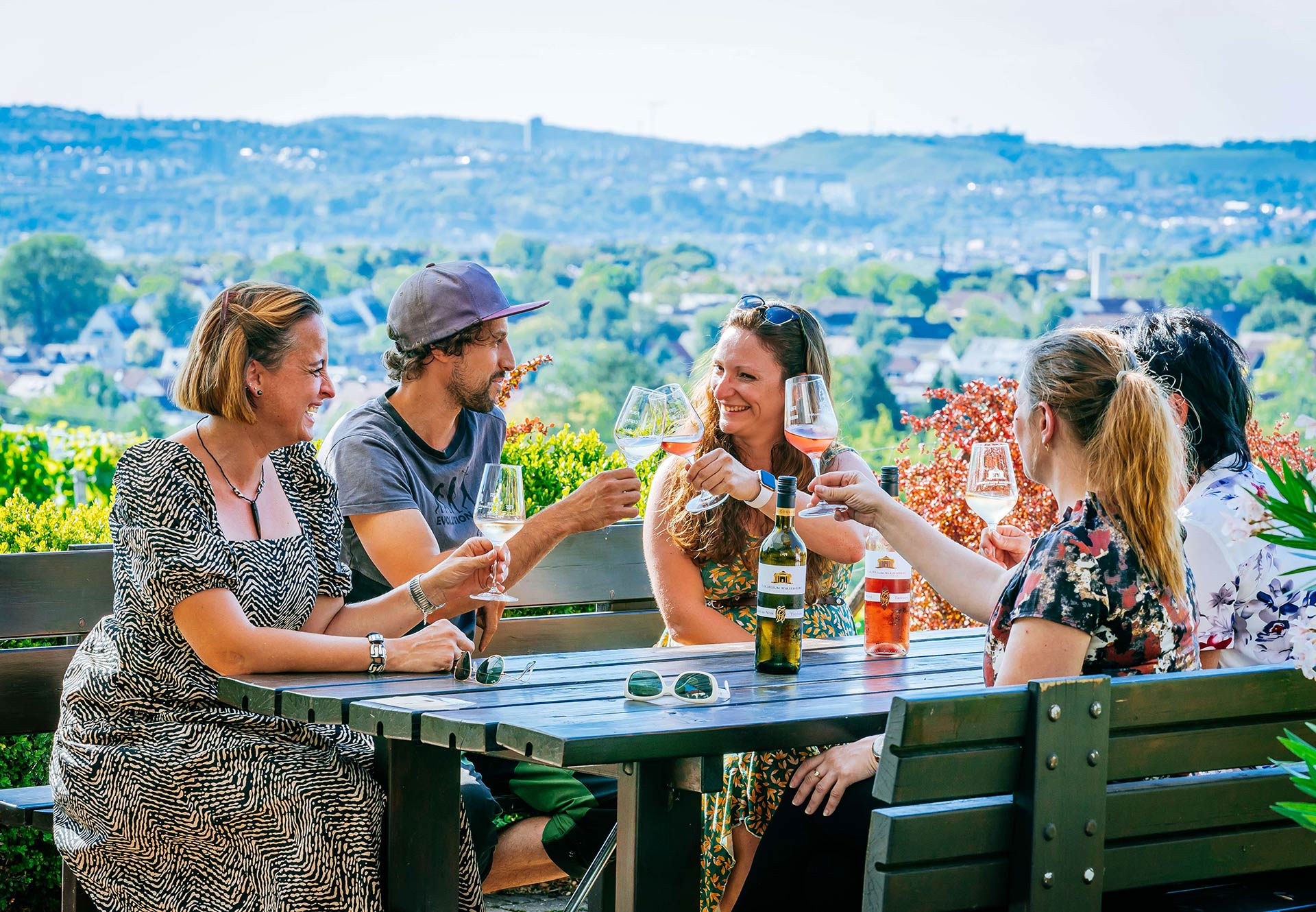 Five people are sitting on a bench and at a table during a wine tour, toasting each other with a full glass of wine.
