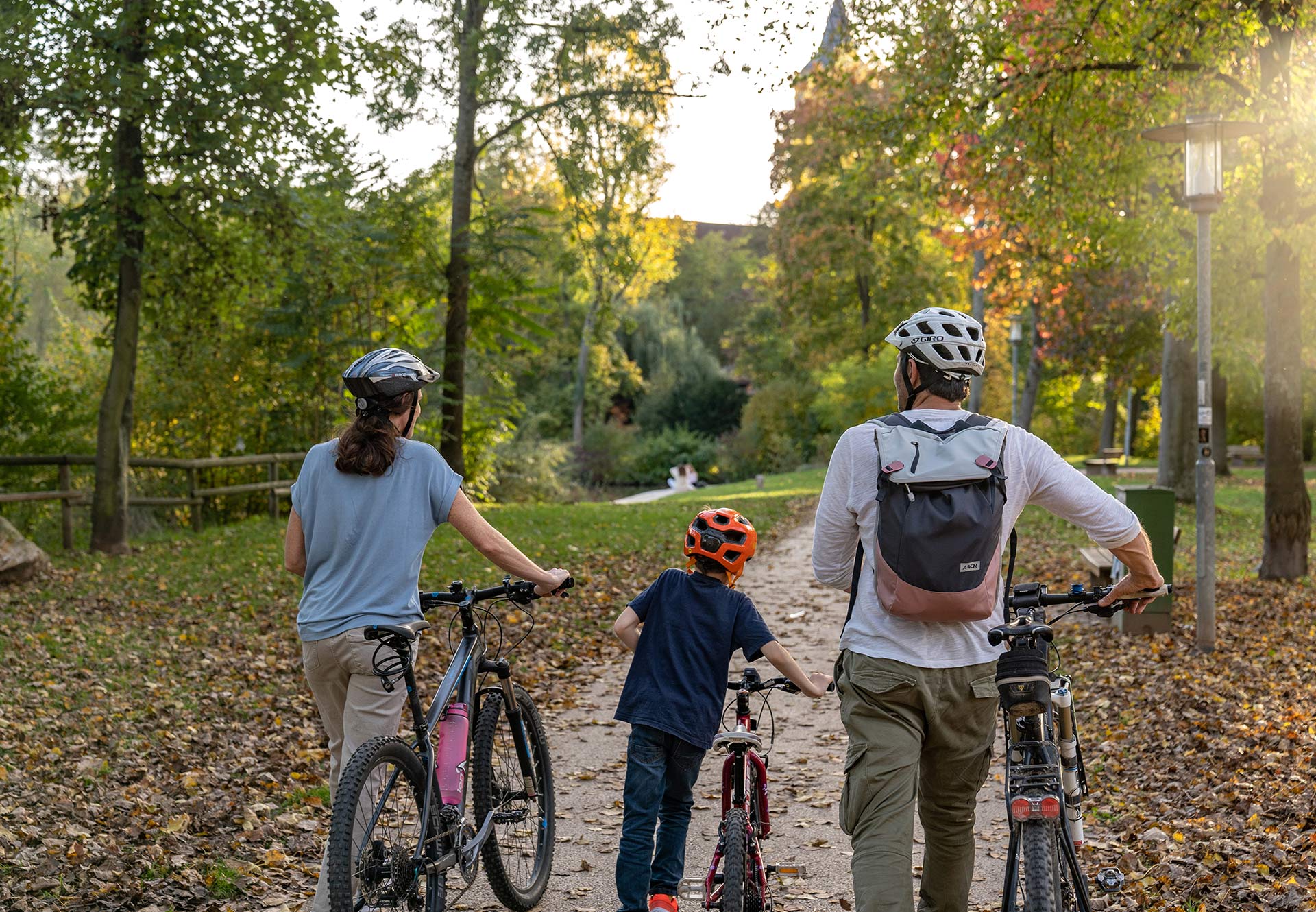 Woman, man and child each push a bicycle and walk along a path through nature.